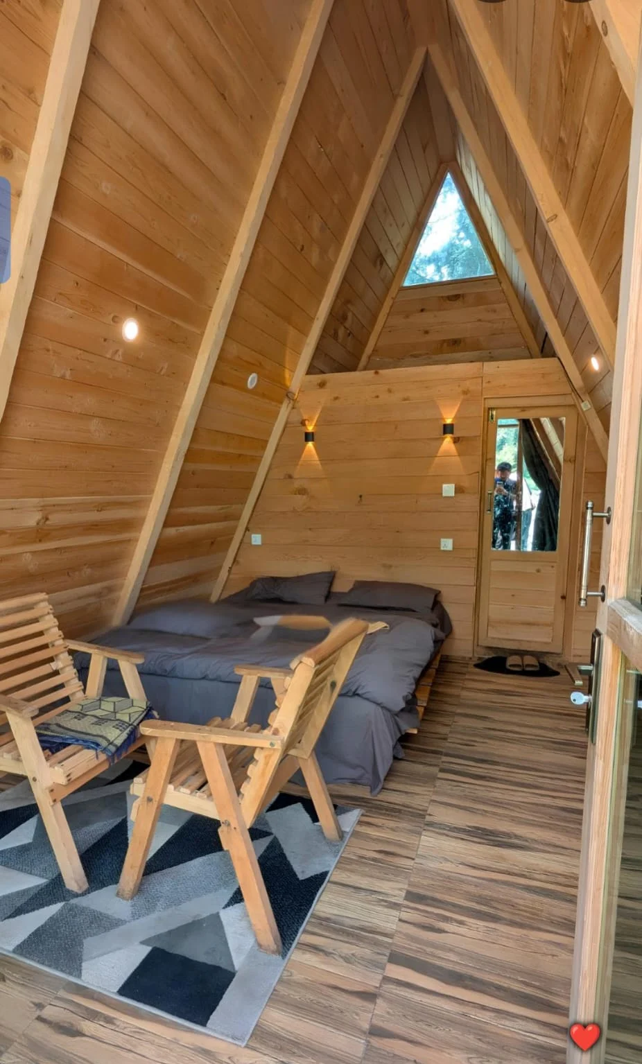 Timber-lined A-frame interior with bed and wooden chairs